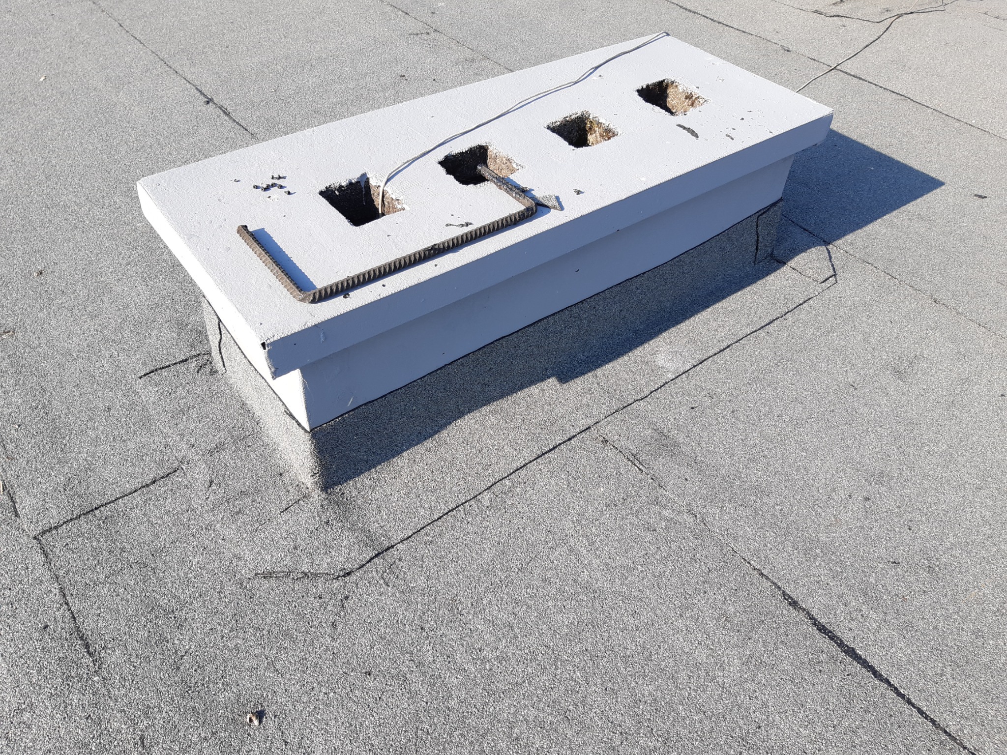 Betonowa podstawa z trzema otworami na dachu pokrytym papą, fragment zbrojenia w jednym z otworów, widoczne przewody.