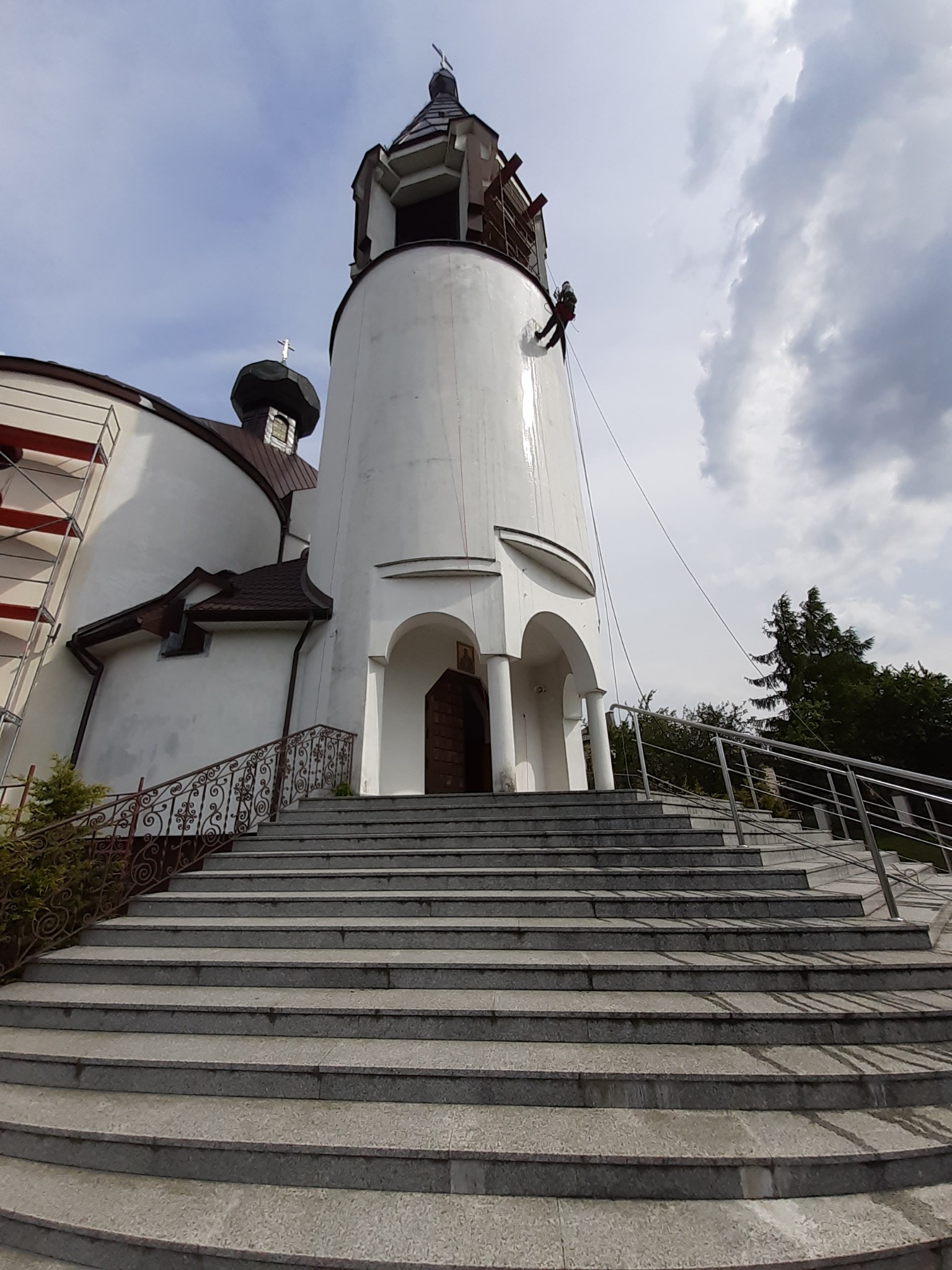 Czyszczenie elewacji kościoła z użyciem technik alpinistycznych, widoczne ślady po umyciu na białej ścianie wieży.