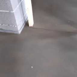 Świeżo wylana, gładka posadzka przemysłowa w szarym odcieniu, widoczne fragmenty ściany z bloczków betonowych i drewnianej konstrukcji szkieletowej.