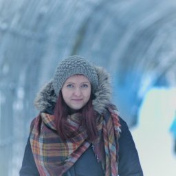 MCF STUDIO - Portret kobiety w zimowej scenerii, ubrana w szarą czapkę z futrzanym pomponem i duży, kraciasty szal, na rozmytym tle tunelu z lodowych konstrukcji.