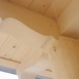 Fragment konstrukcji drewnianej z okrągłym słupem i dekoracyjnymi wycięciami, widok od dołu na jasne drewno.