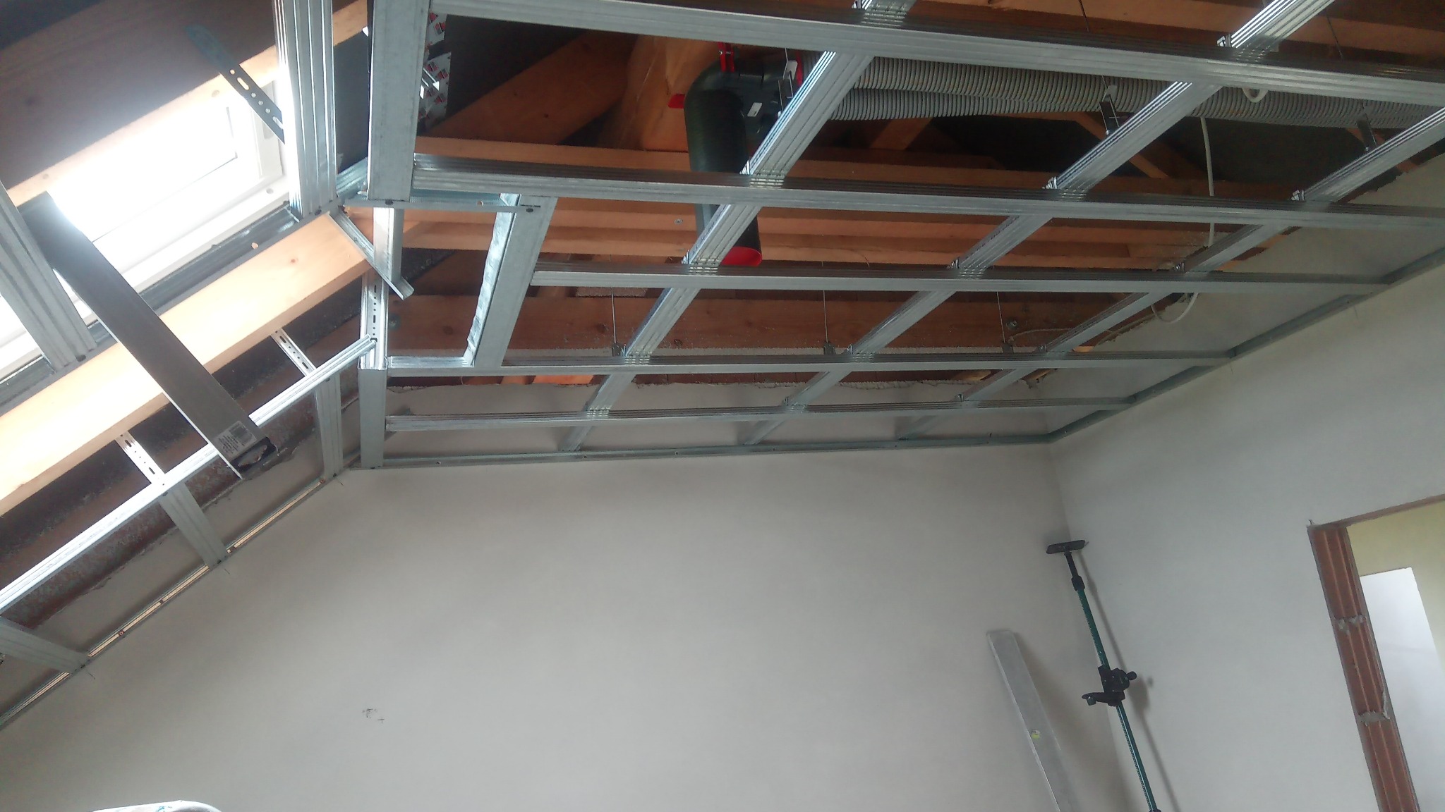 Stelaż z profili metalowych pod zabudowę sufitu podwieszanego na poddaszu, widoczne elementy wentylacji i okno dachowe.