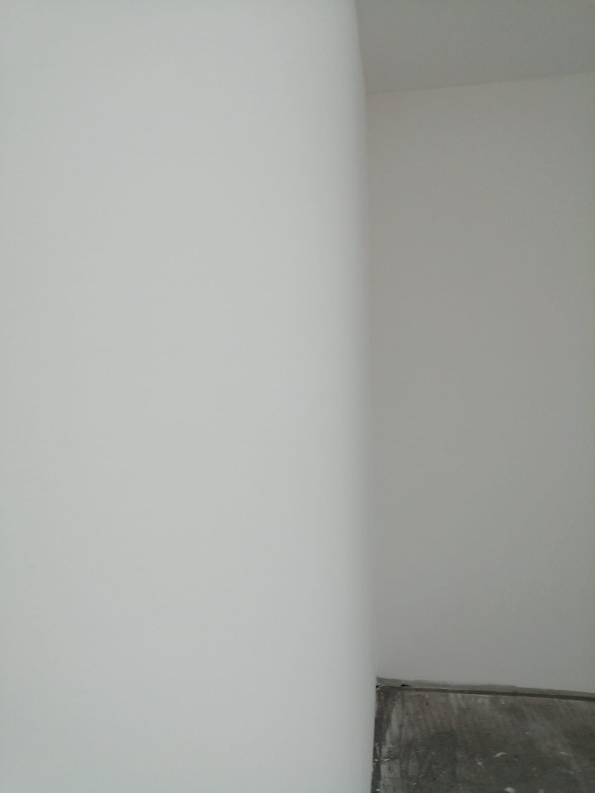 Wnętrze po świeżym, jednolitym malowaniu na biało, widoczny fragment podłogi przy ścianie.