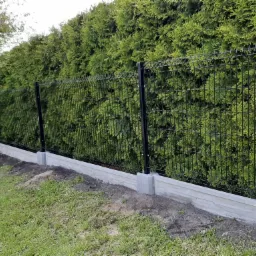 Nowoczesne ogrodzenie panelowe z podmurówką betonową na tle gęstego żywopłotu z tui.