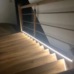 Drewniane schody z podświetleniem LED wzdłuż stopni i metalową balustradą