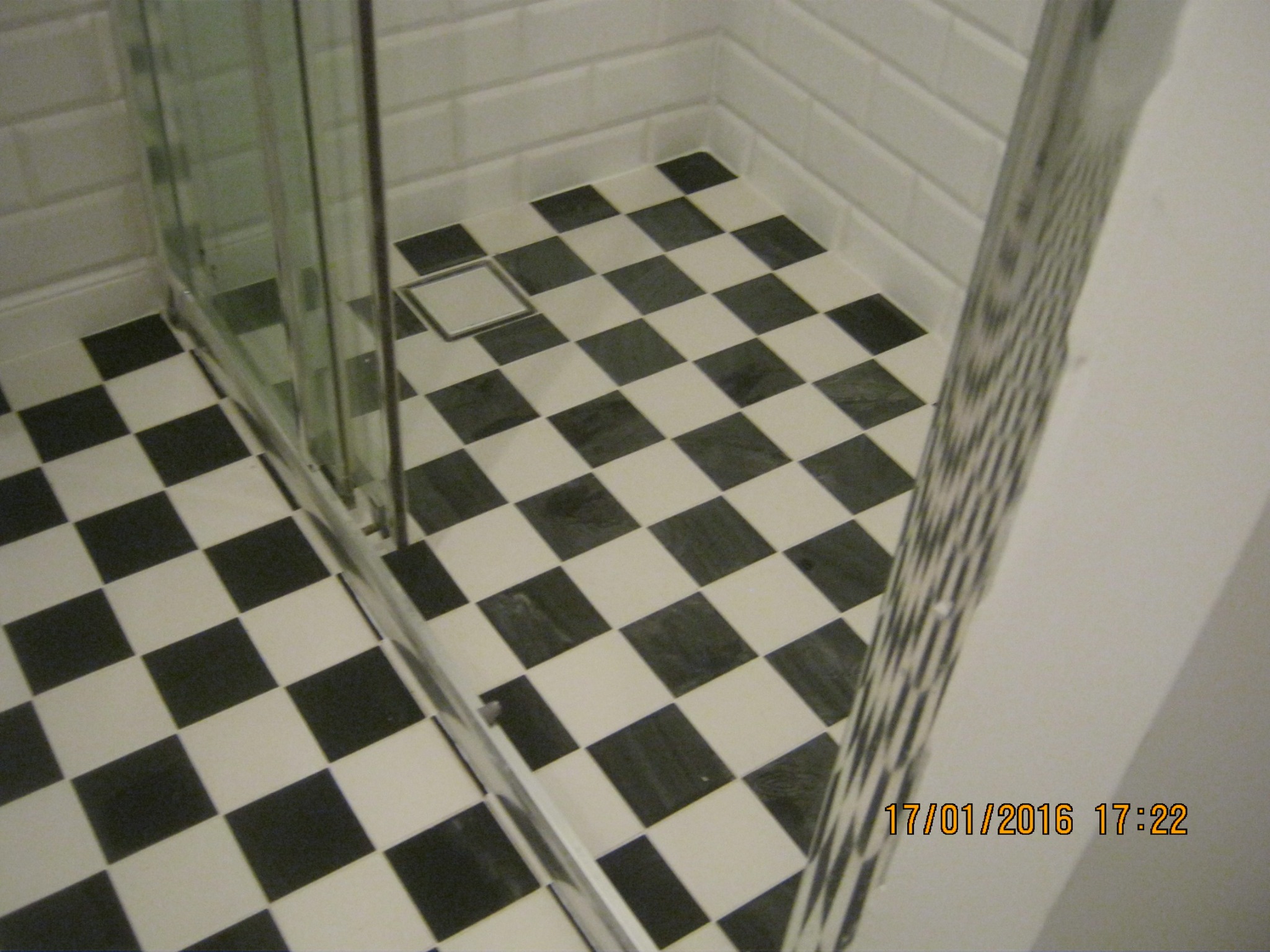 Wykończona kabina prysznicowa z czarno-białą szachownicą na podłodze i białymi płytkami typu metro na ścianach.