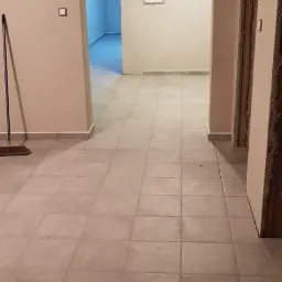 Wykończone wnętrze: beżowe płytki podłogowe w nowym mieszkaniu, widok na przedpokój z pomalowanymi ścianami i otwartymi drzwiami.