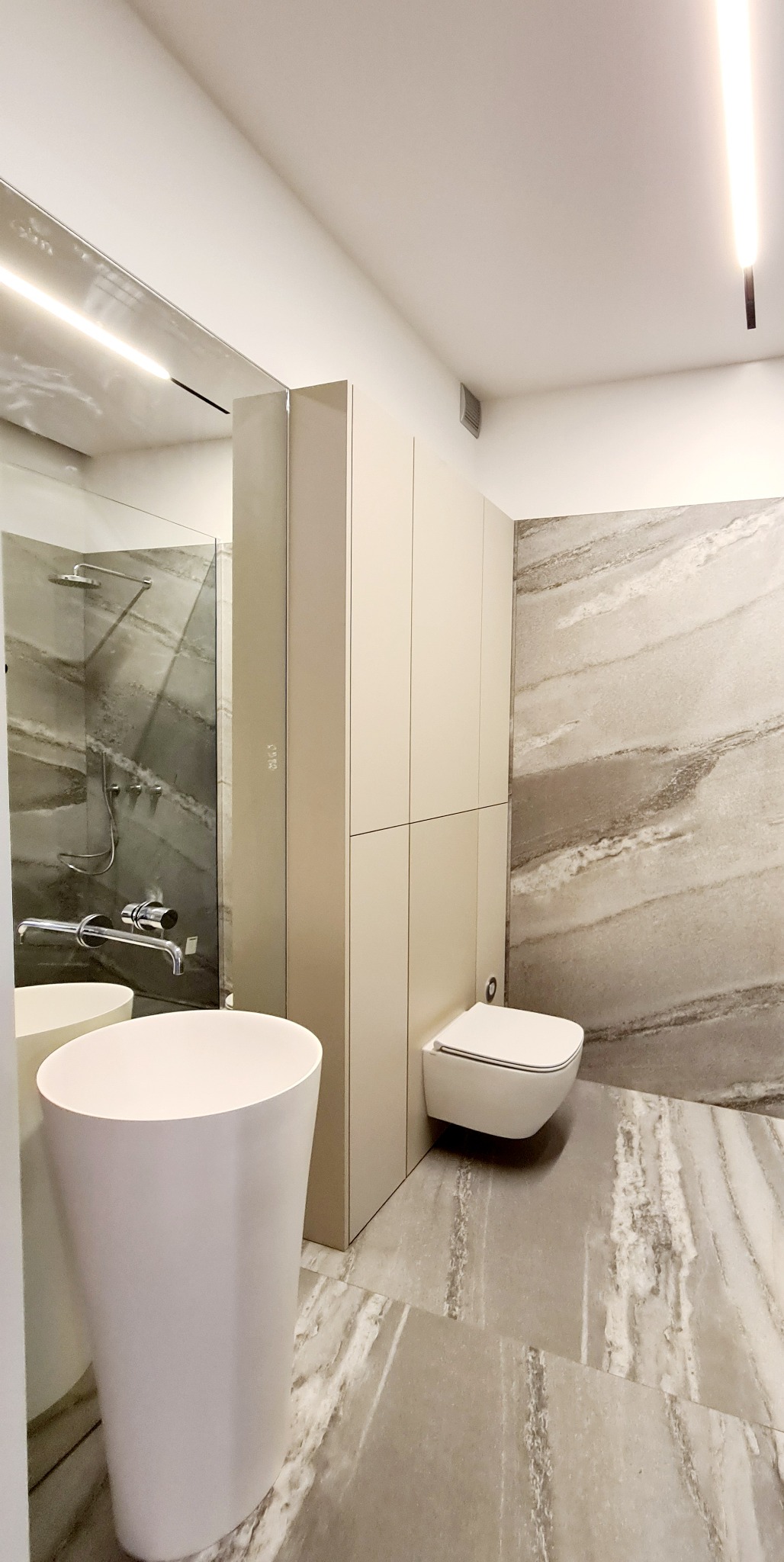 Nowoczesna łazienka z umywalką wolnostojącą, podwieszaną toaletą i płytkami imitującymi marmur, oświetlenie LED.