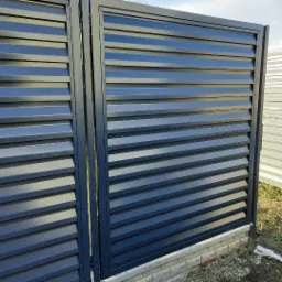 Nowoczesna, antracytowa brama wjazdowa z poziomymi panelami lamelowymi, zamontowana na niskim murku z cegły klinkierowej, widok z bliska.