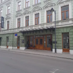 Odnowiona elewacja kamienicy z dekoracyjnymi sztukateriami i drewnianą stolarką okienną, widoczny szyld hotelu i ozdobna latarnia uliczna