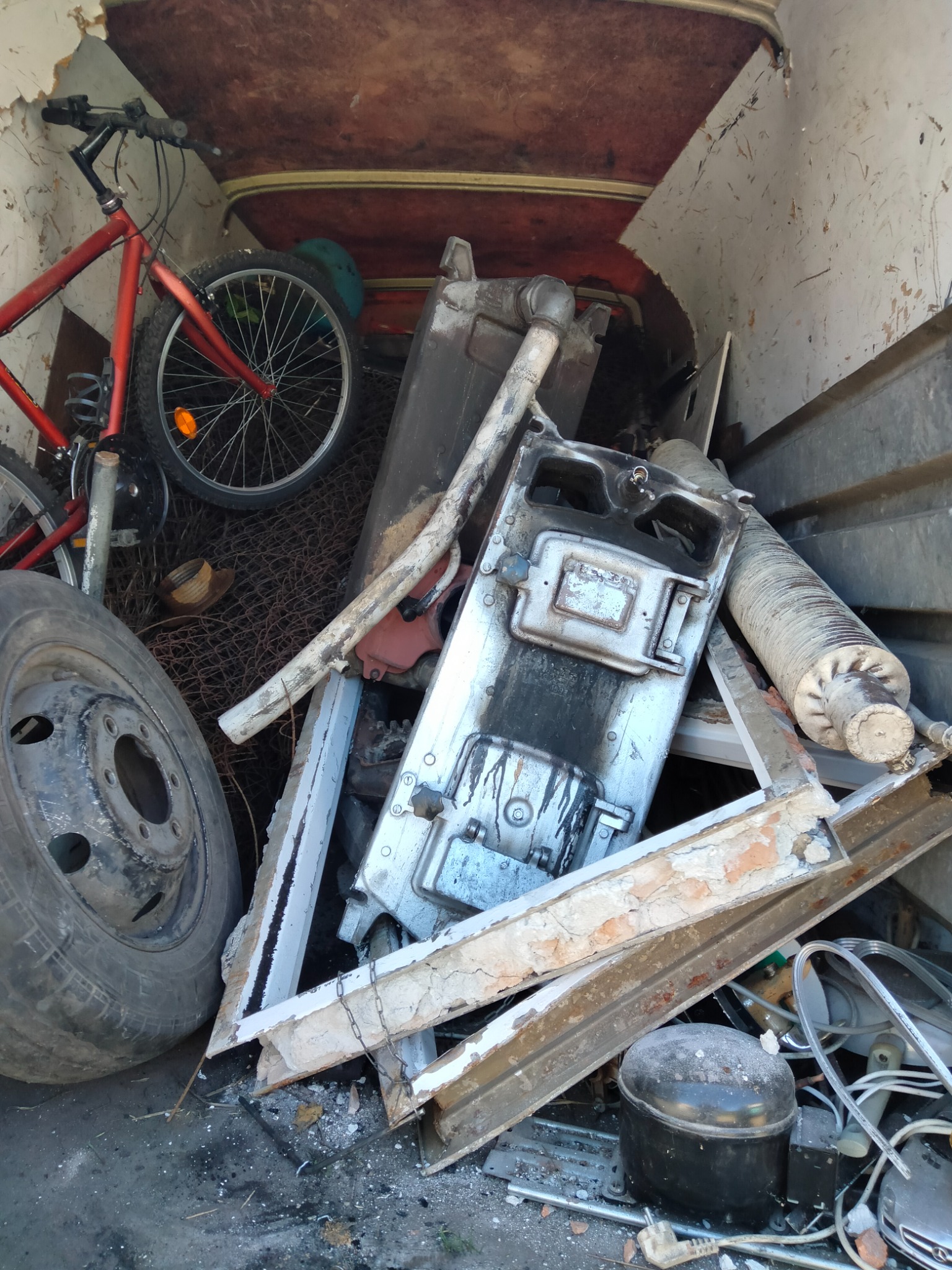 Wnętrze przestrzeni ładunkowej wypełnione różnorodnymi przedmiotami: rower, opona samochodowa, elementy metalowe przypominające fragmenty pieca, gruz i inne przedmioty.