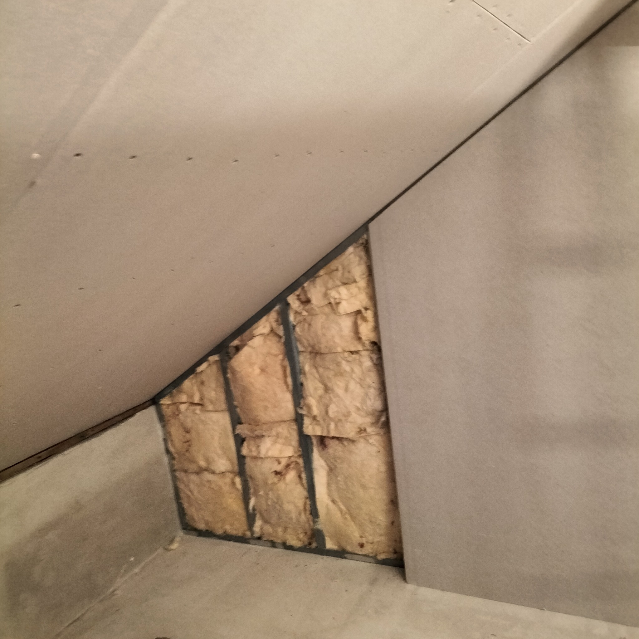 Skośna ściana poddasza w trakcie ocieplania wełną mineralną, widoczne profile metalowe i płyty gipsowo-kartonowe.