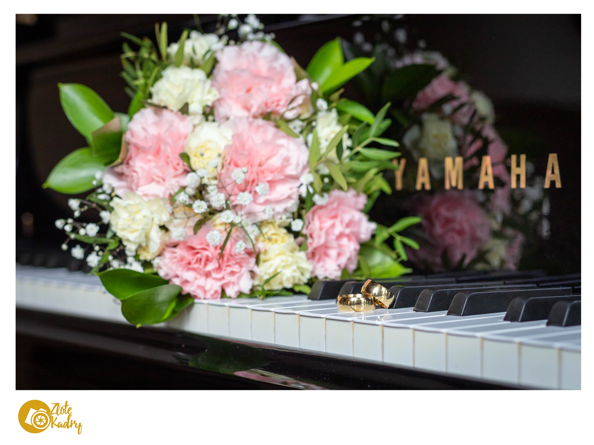 Bukiet różowych i białych goździków oraz obrączki na klawiszach czarnego fortepianu Yamaha.