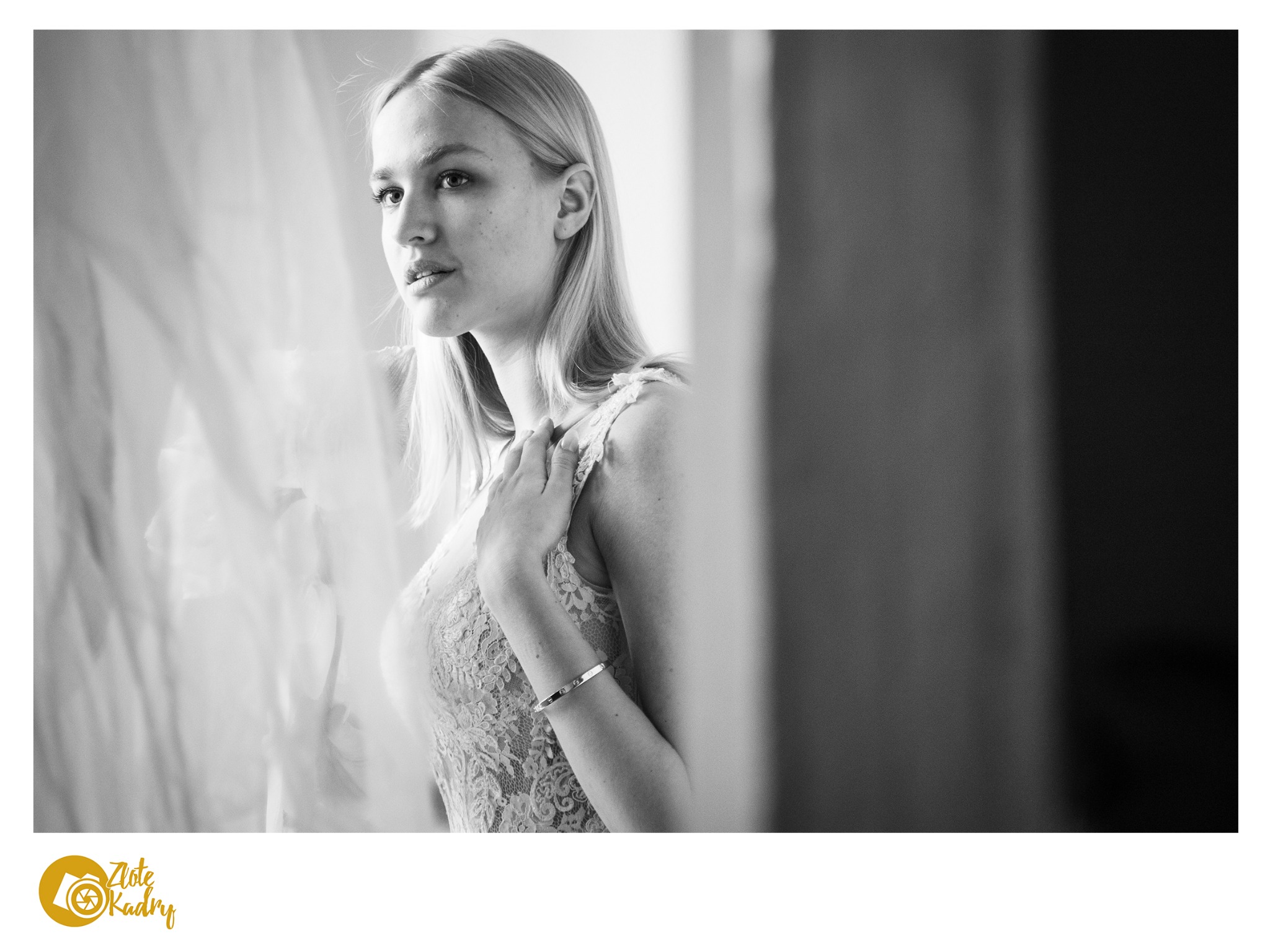 Portret kobiety w koronkowej sukience, z bransoletką na ręce, spoglądającej w lewo, w czerni i bieli.