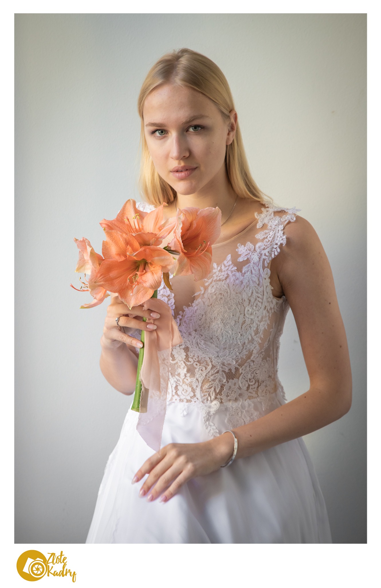 Portret panny młodej w koronkowej sukni, trzymającej bukiet amarylisów w odcieniach brzoskwini i różu, z subtelną biżuterią.