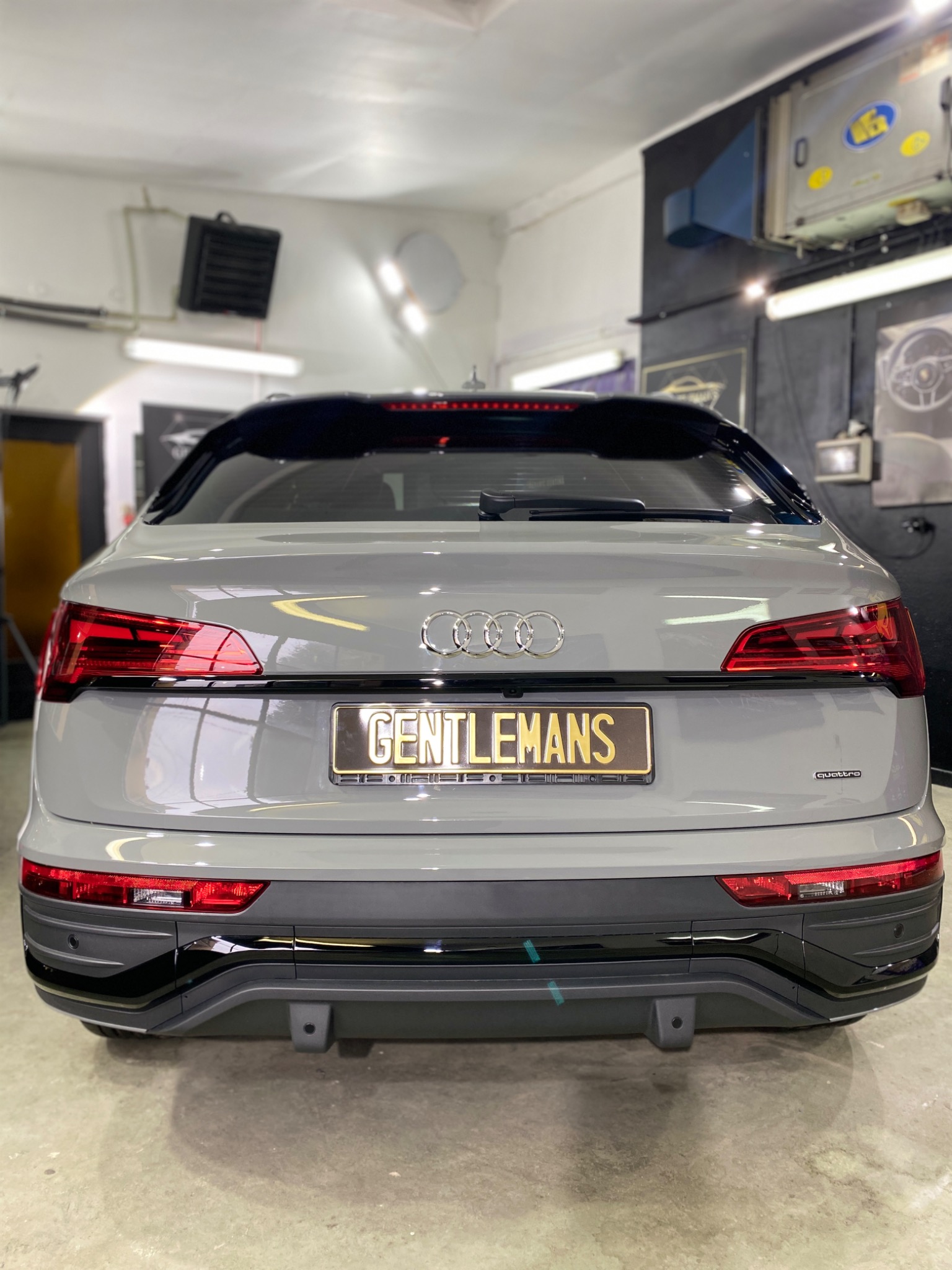 Szary samochód Audi Q5 z tablicą rejestracyjną GENTLEMANS, widziany z tyłu w warsztacie, z widocznymi światłami i logo Quattro.