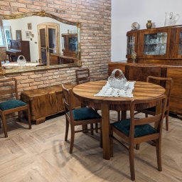 Lech-Bud - Salon z odrestaurowanymi meblami w stylu art deco: okrągły stół z kryształowym koszyczkiem na serwecie, krzesła z zielonym obiciem, kredens i komoda z fornirem oraz lustro w złotej ramie...