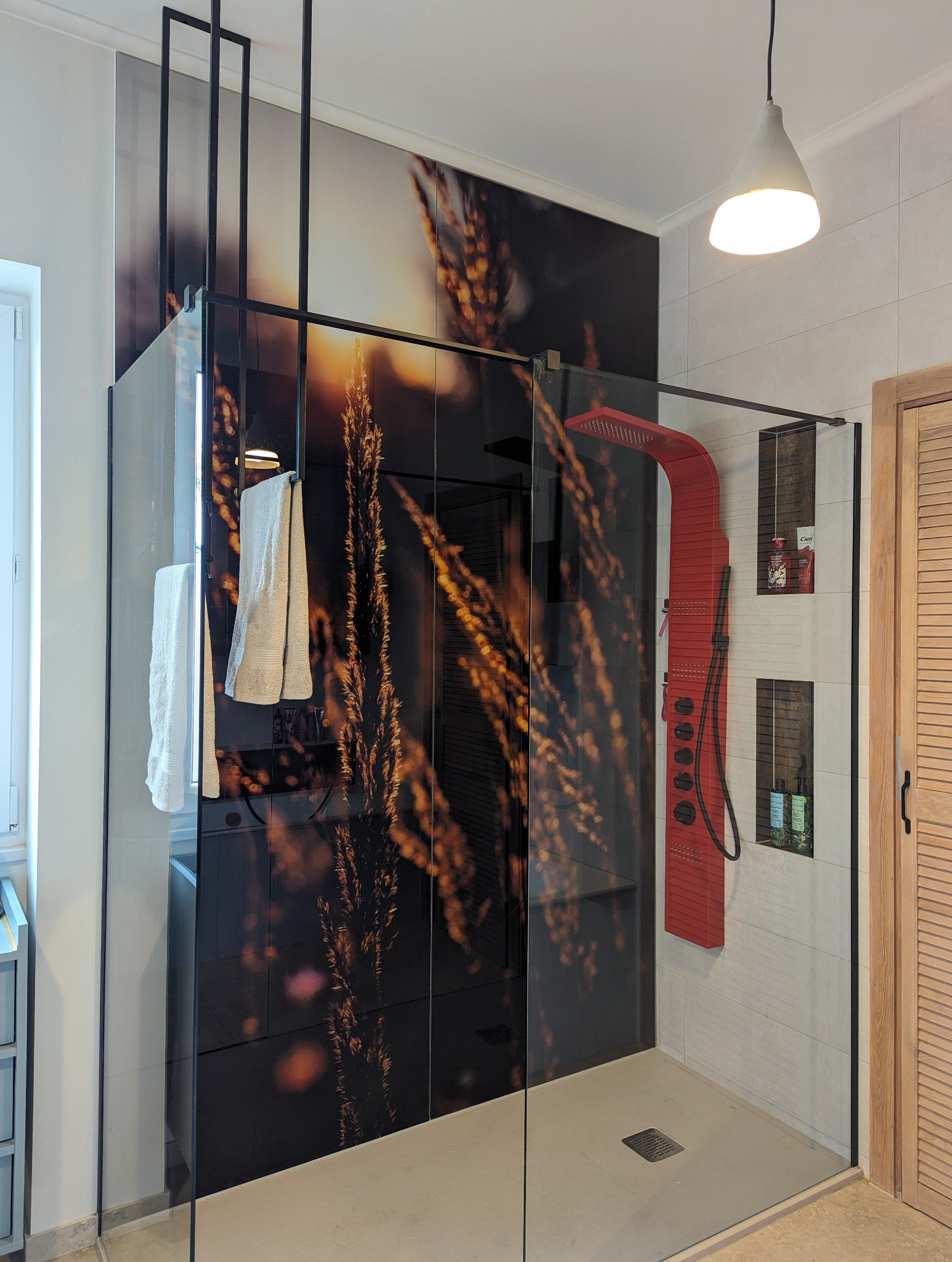 Nowoczesna kabina prysznicowa z czarnymi profilami, szklanymi ścianami z motywem roślinnym, czerwonym panelem natryskowym i wnękami na kosmetyki.