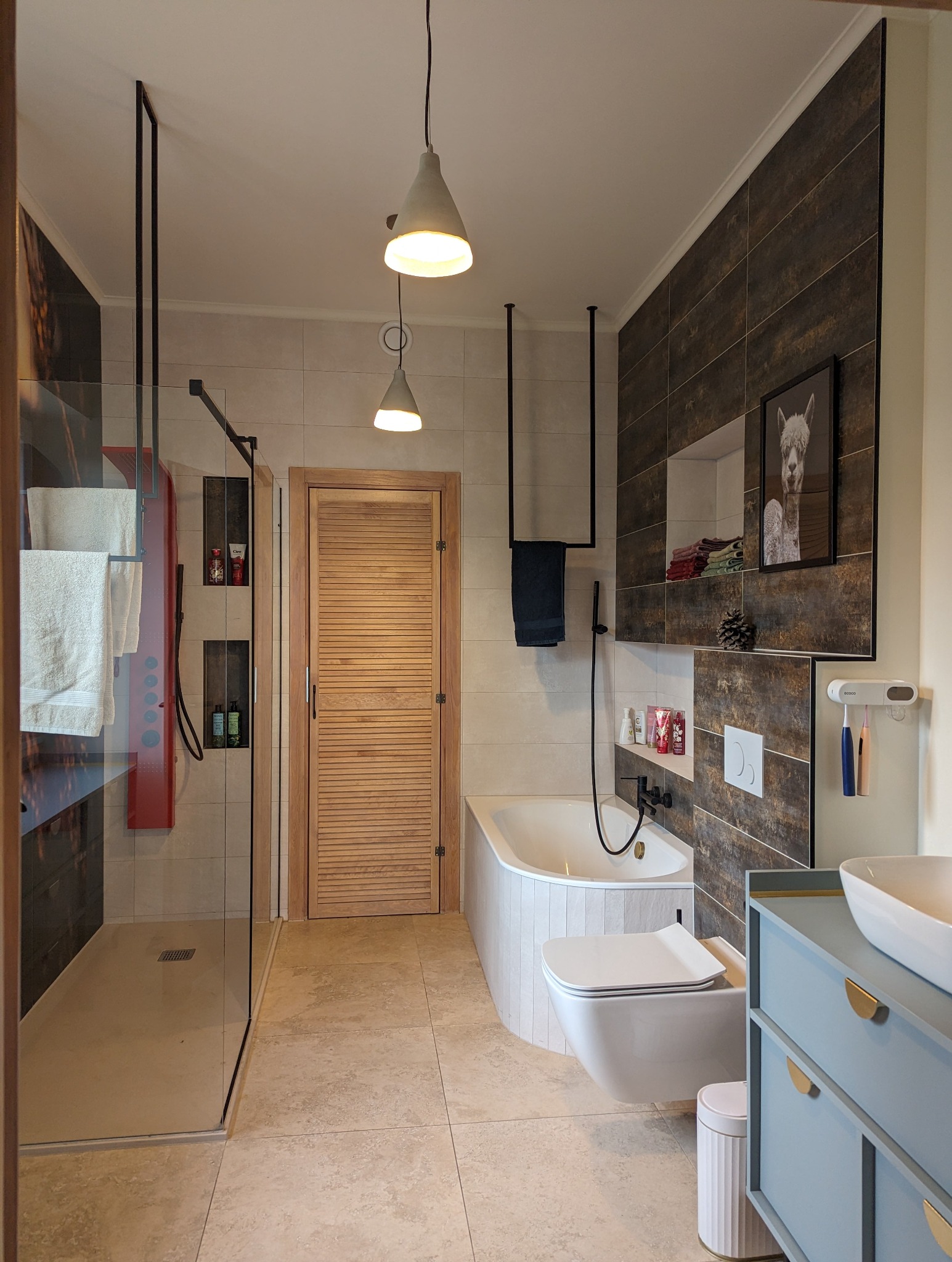 Nowoczesna łazienka z kabiną prysznicową typu walk-in, wanną obudowaną pionowymi panelami, wiszącą toaletą i szafką umywalkową w kolorze pastelowego błękitu z złotymi uchwytami.