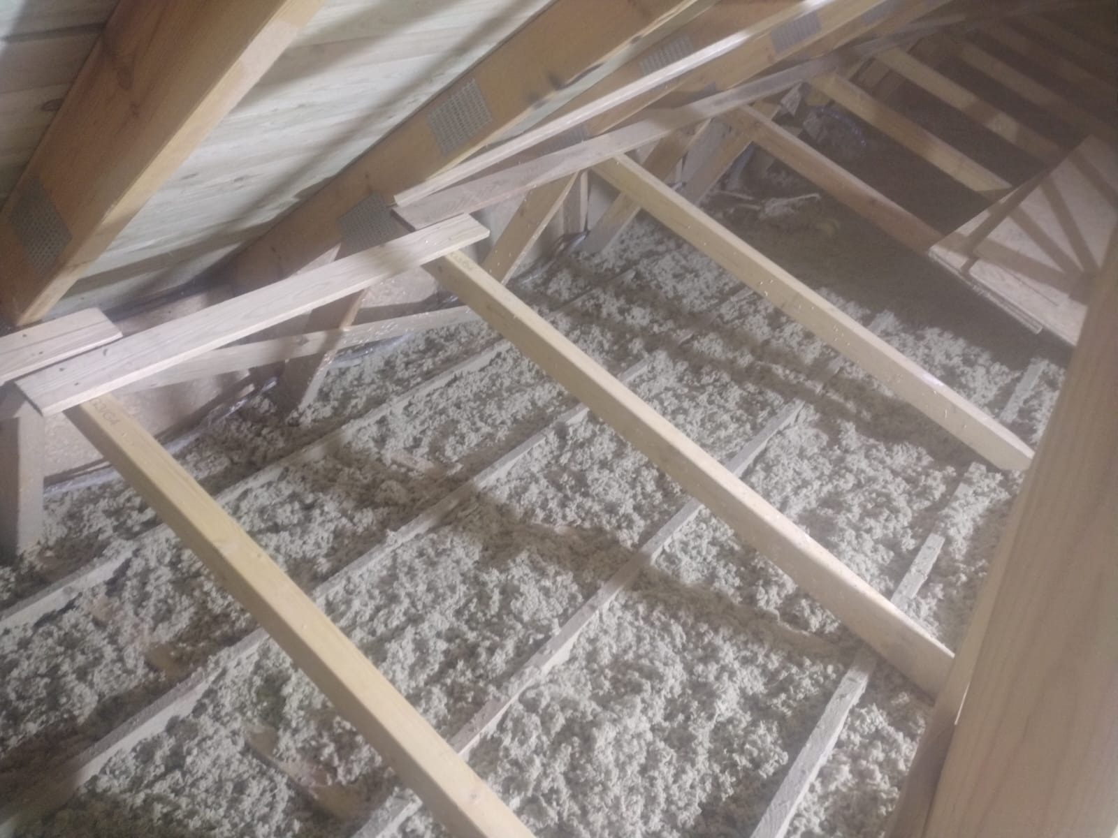 Poddasze z drewnianą konstrukcją i izolacją z wełny mineralnej, widok z góry na nierównomiernie rozłożony materiał izolacyjny pomiędzy krokwiami.