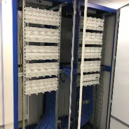 Otwarta szafa serwerowa w kolorze niebiesko-białym, zawierająca panele krosownicze z dużą ilością niebieskich kabli sieciowych uporządkowanych w wiązki.