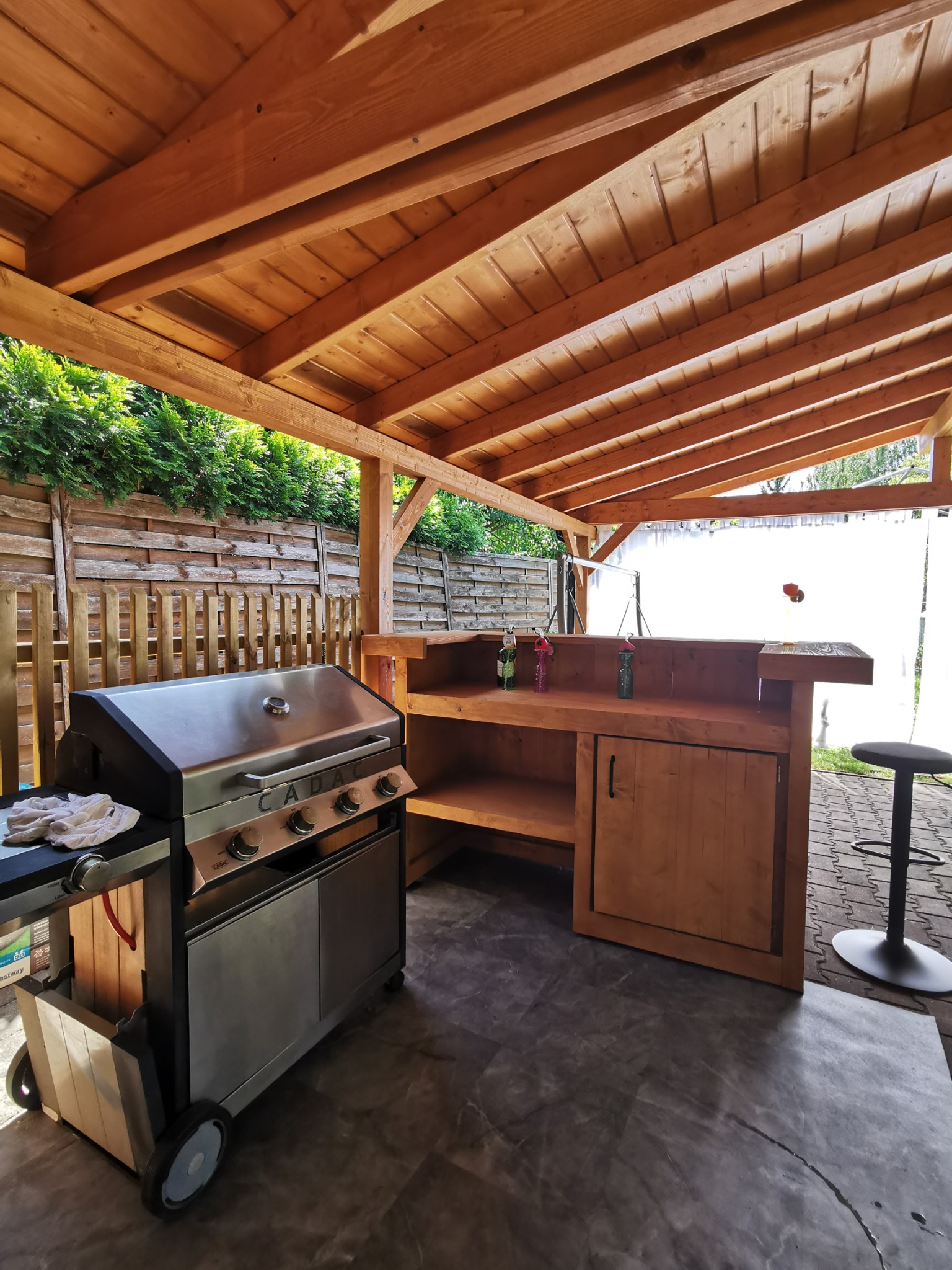 Drewniana altana z grillem i barkiem, idealna na letnie spotkania. Widoczne detale konstrukcji i wyposażenia.