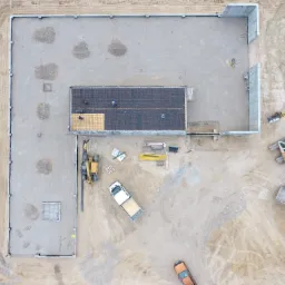 Widok z drona na plac budowy hali magazynowej z częścią biurową w Iławie, widoczne fundamenty, zbrojenie i pracujący robotnicy.