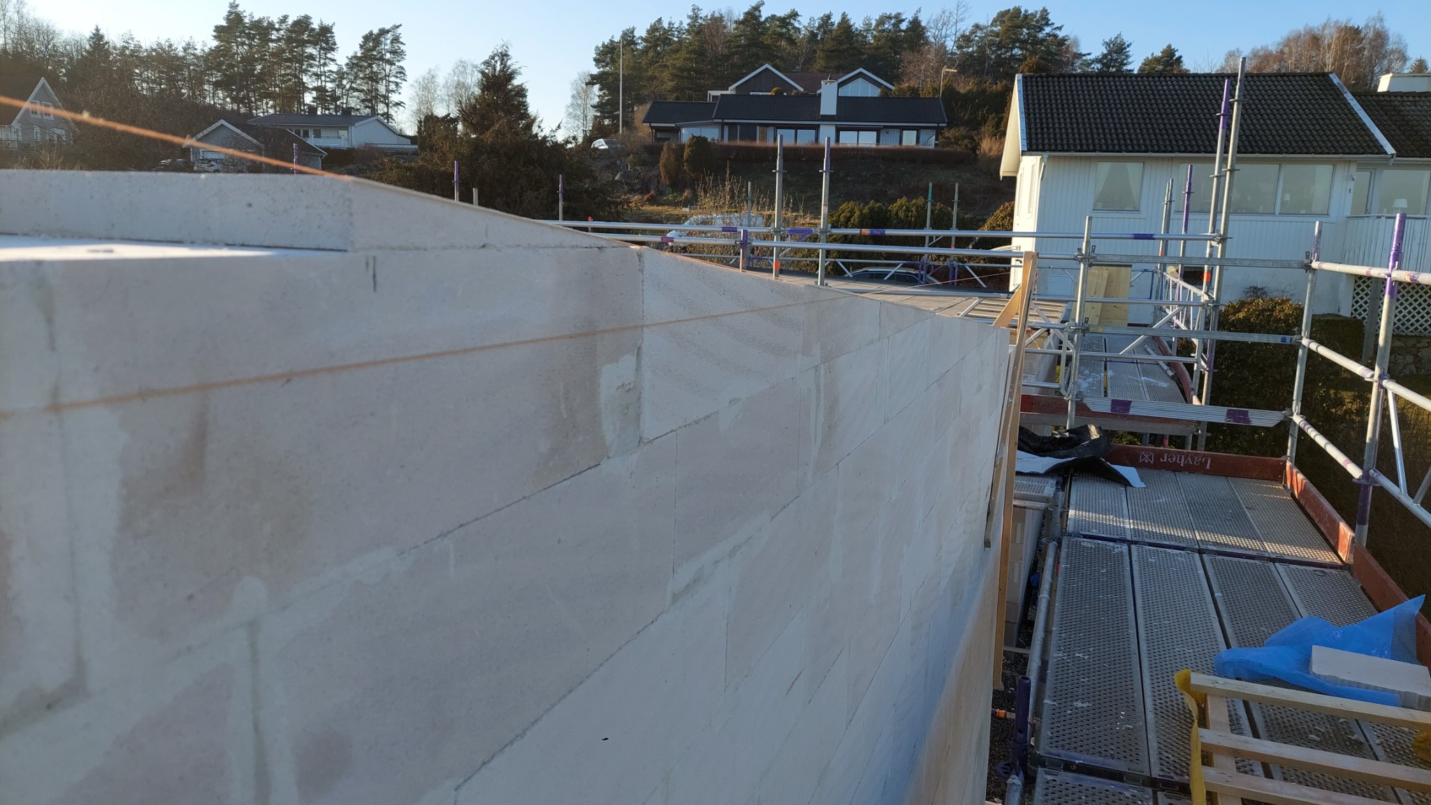 Ściana z betonu komórkowego w trakcie budowy, widoczne sznurki wyznaczające linię, rusztowanie Layher w tle.