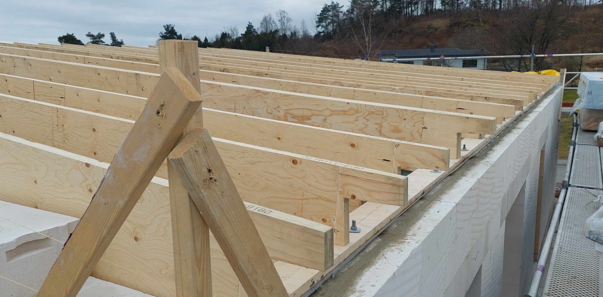 Konstrukcja drewniana dachu z belek i płyt OSB, zamocowana do muru z betonu komórkowego, widok z góry na wczesnym etapie budowy.