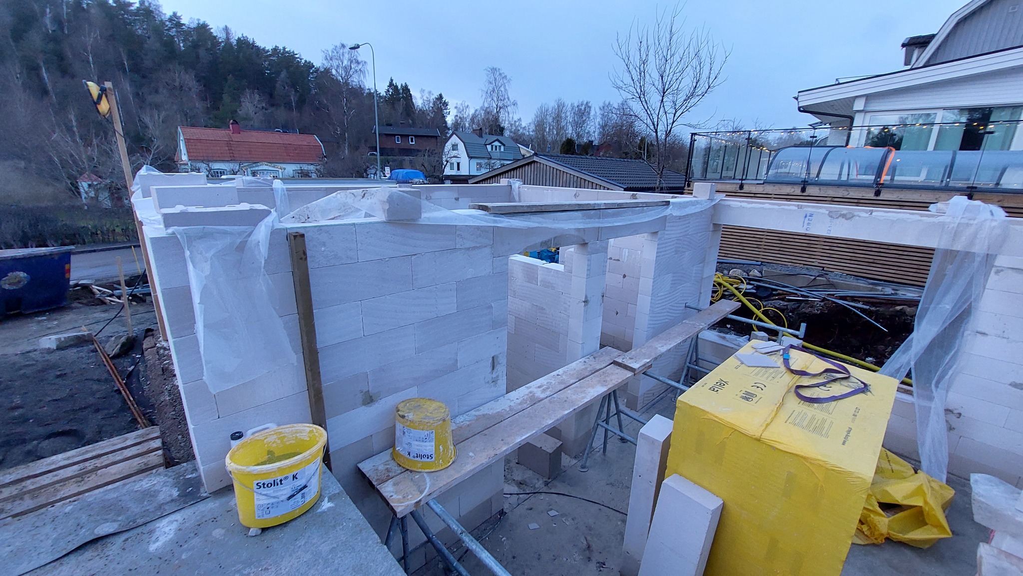 Wznoszenie ścian z bloczków z betonu komórkowego na tle zabudowy jednorodzinnej i zalesionego wzgórza o zmierzchu.