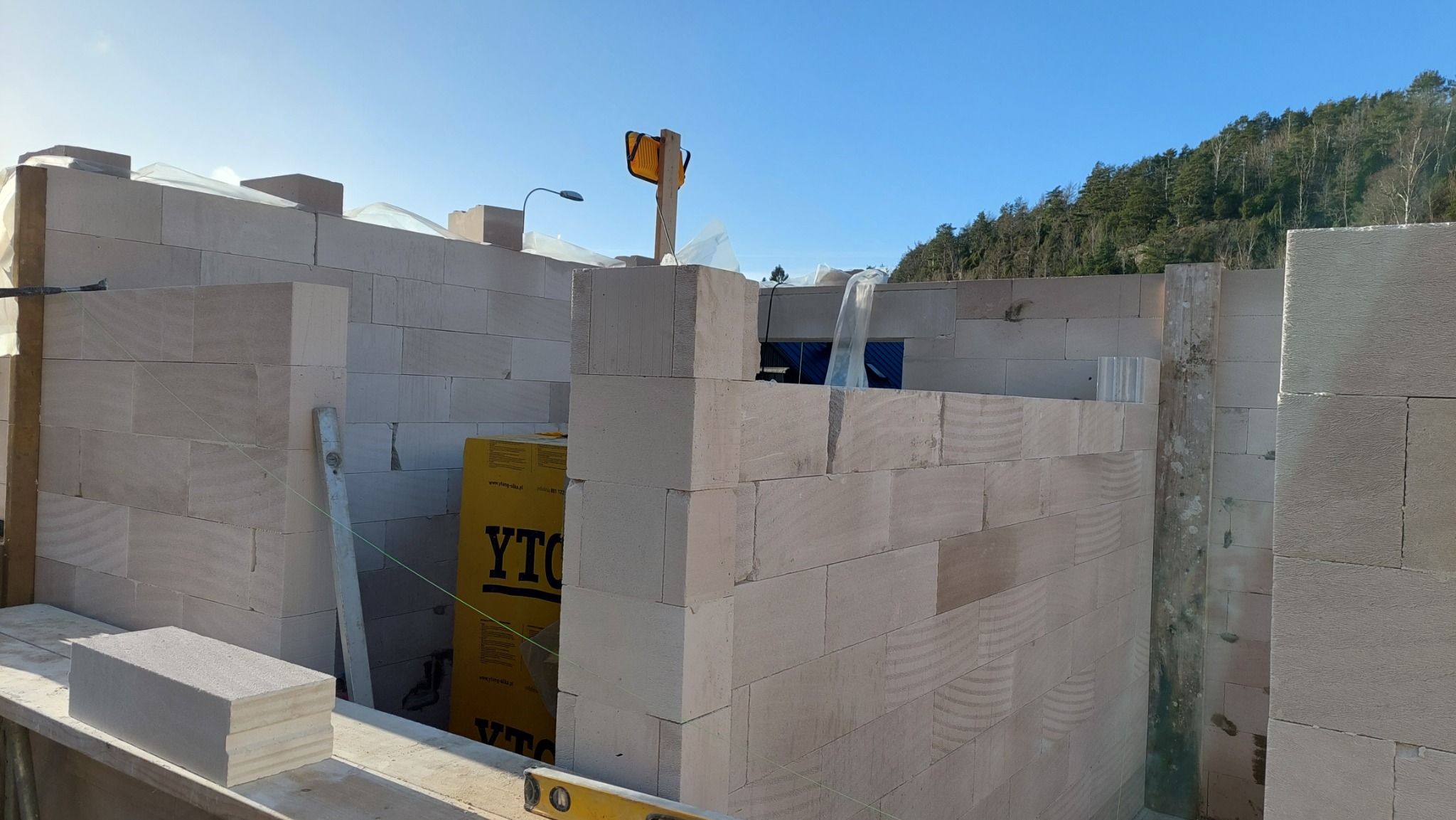 Wznoszenie ścian z bloczków z betonu komórkowego YTONG, widoczny fragment budynku w stanie surowym otwartym, narzędzia murarskie i lampa budowlana.