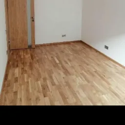 Jasny parkiet ułożony w pokoju w Gliwicach, widoczna drewniana ościeżnica drzwiowa i gniazdka elektryczne na białych ścianach.