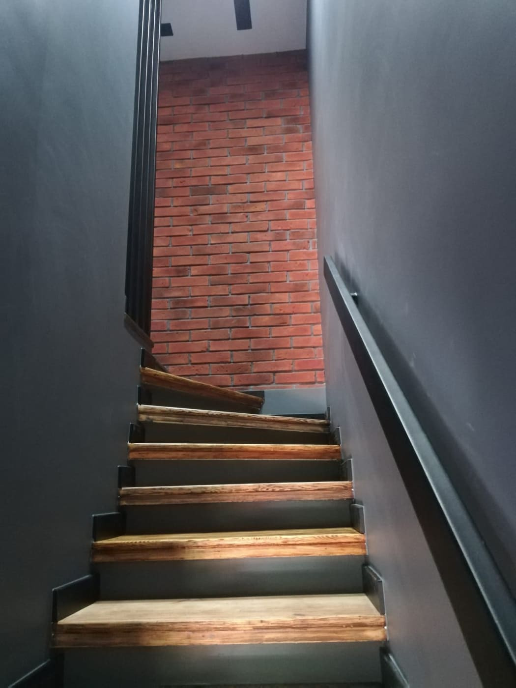 Schody drewniane z metalowymi elementami i ceglaną ścianą w tle, Kielce. Ujęcie od dołu, podkreślające kontrast materiałów i nowoczesny design.