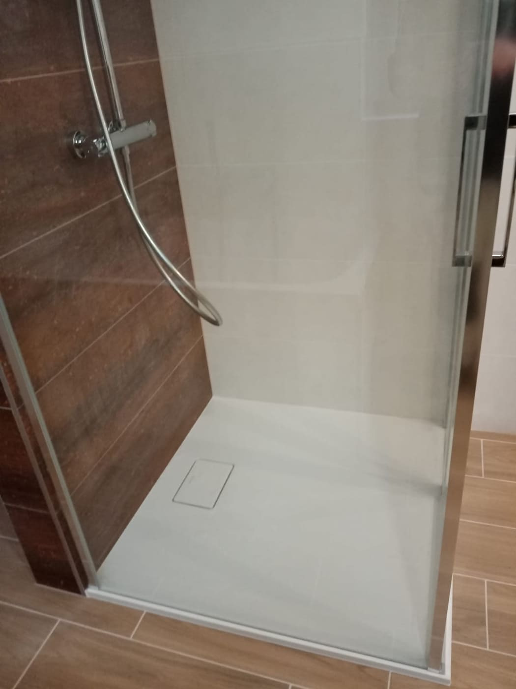 Nowoczesna kabina prysznicowa z brązowymi panelami ściennymi imitującymi drewno i jasnymi płytkami, z odpływem liniowym w posadzce.