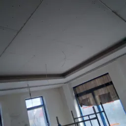 Montaż sufitu podwieszanego z płyt karton gips, widoczne profile, instalacja elektryczna, okna zabezpieczone folią malarską.