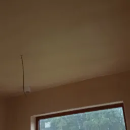 Gładki, świeżo otynkowany sufit w Złotowie, widoczny kabel oświetleniowy zwisający z puszki. Za oknem widoczny krajobraz z zaparkowanym busem firmy.