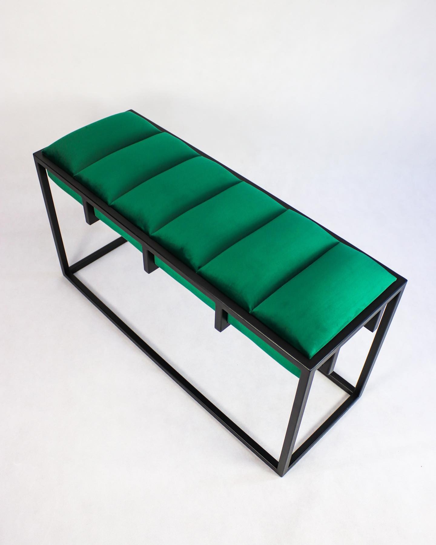 Metalowa ławka z ciemnozielonym, tapicerowanym siedziskiem podzielonym na pięć segmentów, na białym tle, z widoczną strukturą spawanych profili.