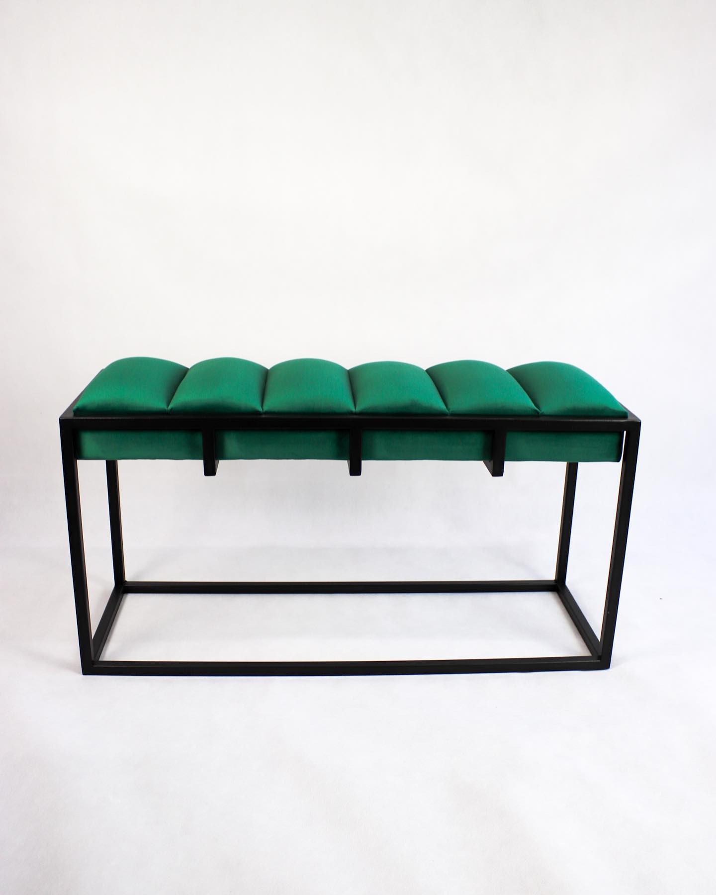 Nowoczesna ławka z siedziskiem z zielonego aksamitu i czarną metalową ramą na białym tle.