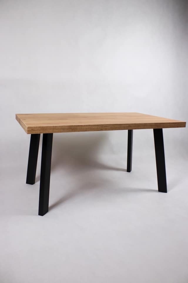 Stół z blatem z płyty laminowanej w kolorze dąb kraft złoty i czarnymi, malowanymi proszkowo nogami o profilu 60x30x2 mm, na jasnym tle.