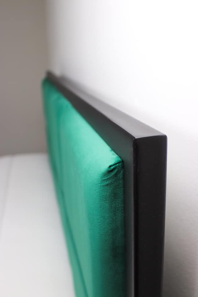 Fragment wezgłowia łóżka z zieloną tapicerką i czarną ramą, widok z boku, ukazujący detale wykończenia.