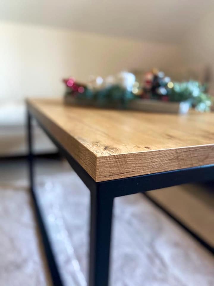 Stół kawowy z drewnianym blatem i czarnymi metalowymi nogami, wykonany na zamówienie w Raszkowie, z dekoracją świąteczną w tle.
