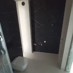 Nowoczesna łazienka z czarnymi płytkami imitującymi marmur, białą ceramiką i jasną podłogą z płytek, widoczna instalacja wodna na ścianie.