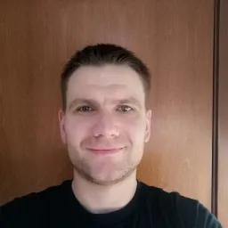 Portret uśmiechniętego mężczyzny na tle brązowych drzwi.