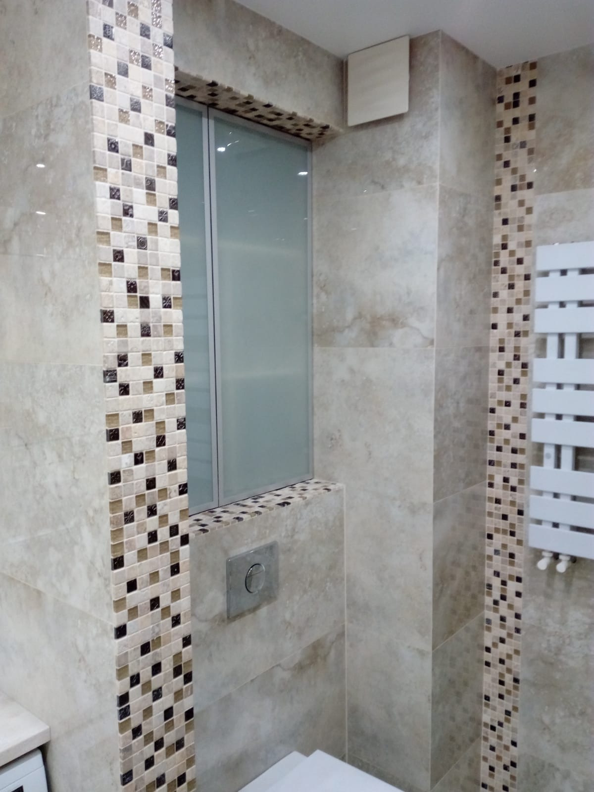 Beżowa łazienka z mozaiką, zabudowaną szafką nad toaletą i grzejnikiem drabinkowym.