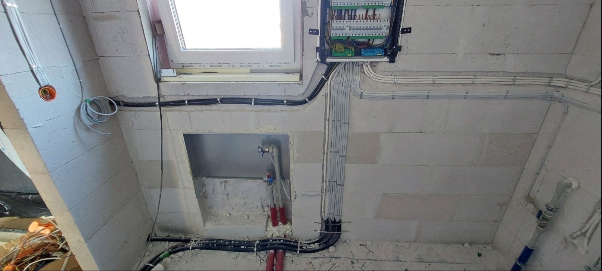 Rozdzielnia elektryczna z poprowadzonymi przewodami w surowym wnętrzu poddasza z oknem dachowym, widoczne kable w peszlach i puszka instalacyjna.