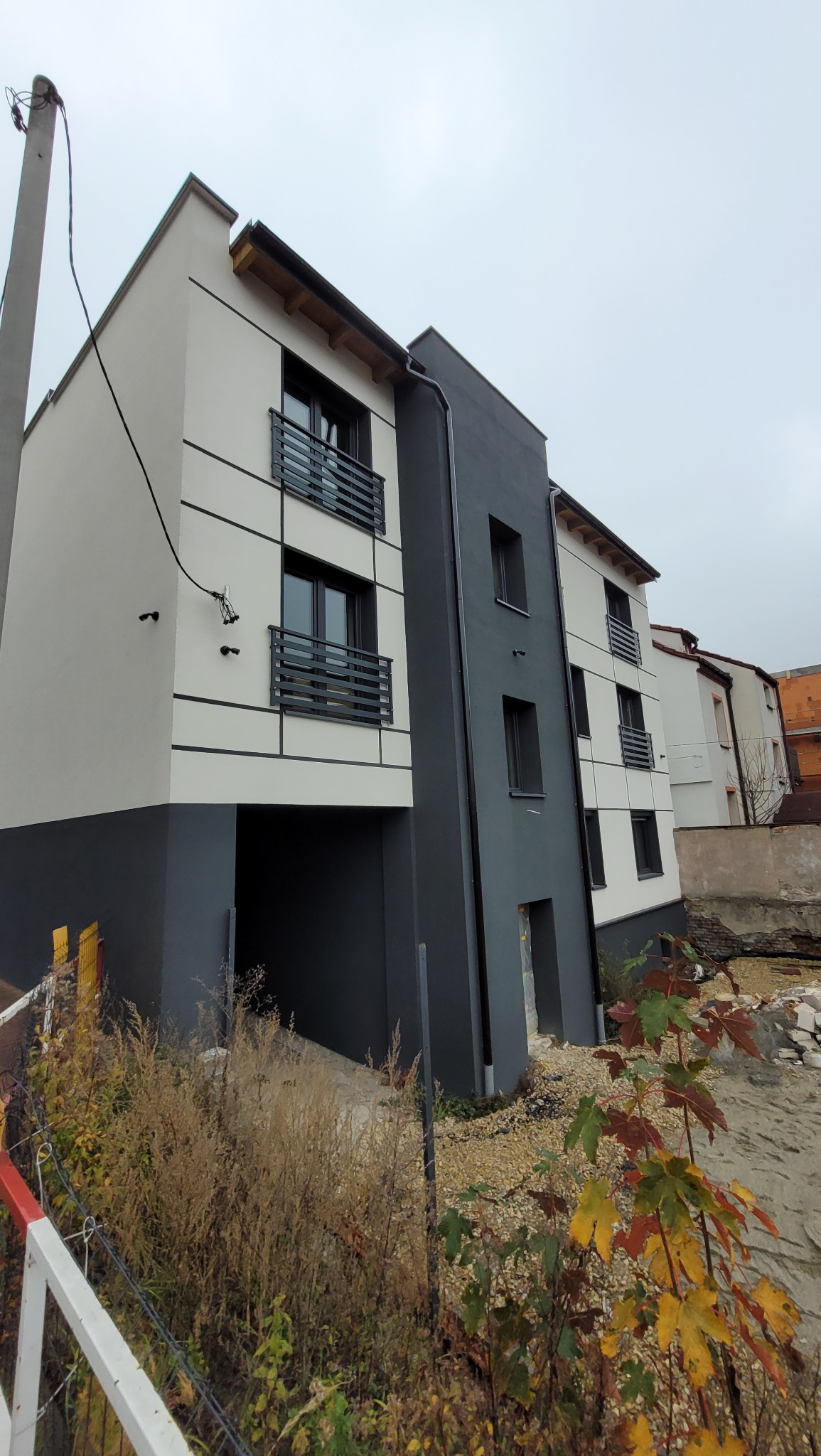 Nowoczesny budynek wielorodzinny w Żorach z balkonami i garażem, wykończony w odcieniach szarości i bieli. Widok z dołu, pochmurne niebo.