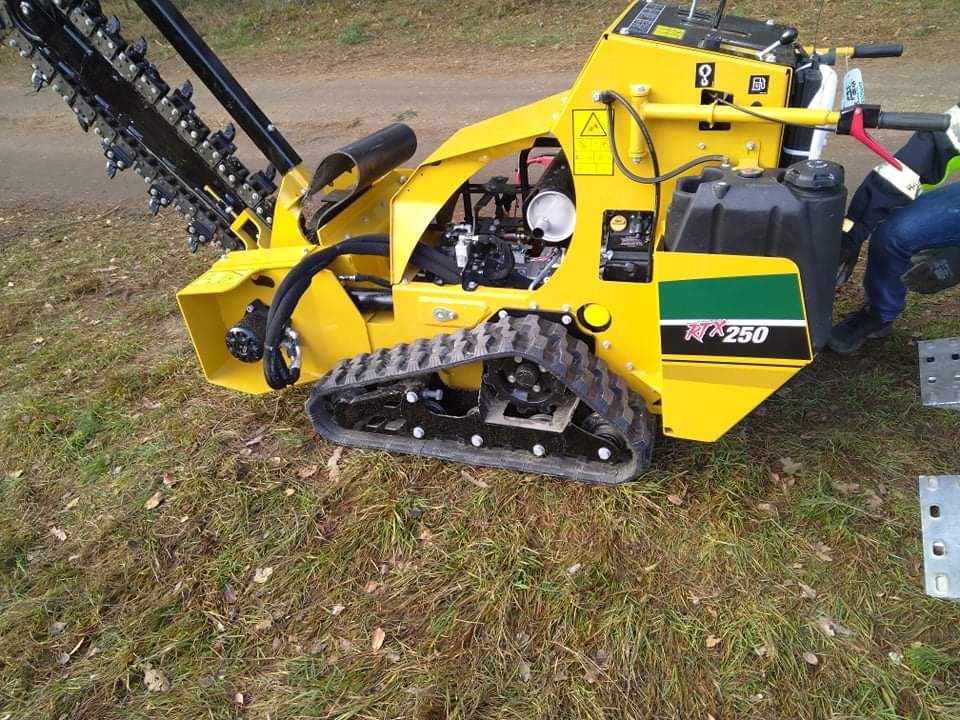 Żółta minikoparka łańcuchowa RTX250 na gąsienicach, widoczna na trawiastym terenie, przygotowana do pracy.
