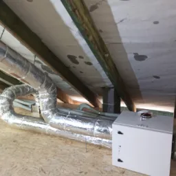 Rekuperator z podłączonymi przewodami wentylacyjnymi w przestrzeni poddasza, widoczne elementy konstrukcji dachu i izolacji.