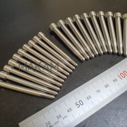 MAKAM Mateusz Pięk - Precyzyjnie wykonane, metalowe trzpienie ułożone obok miarki, prezentujące dokładność obróbki w serwisie elektronarzędzi. Detal w zbliżeniu na czarnym tle.