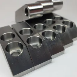 Szereg metalowych, obrobionych elementów z otworami i wycięciami, ułożonych na białym tle, ukazujących precyzyjną obróbkę skrawaniem.